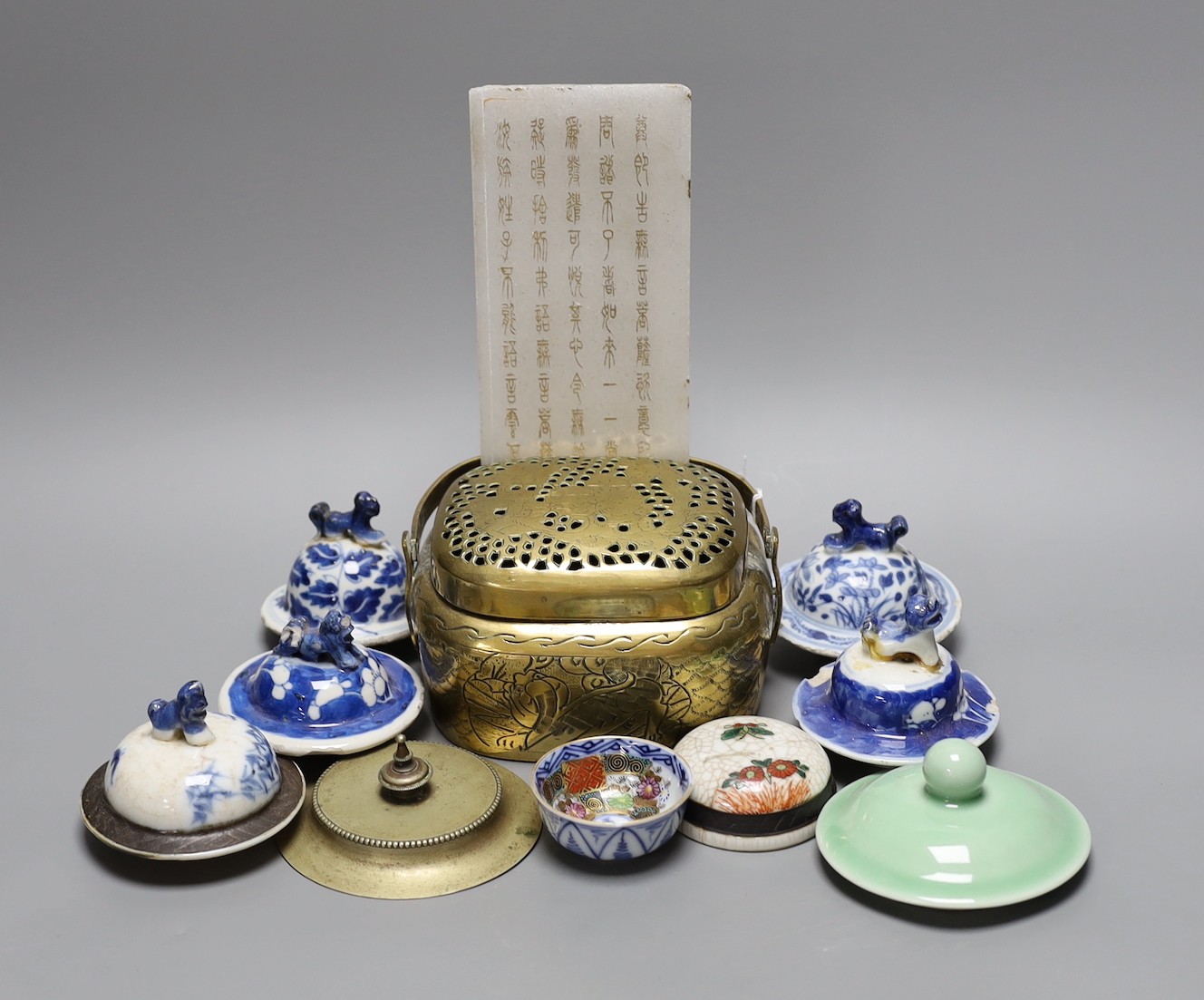 A collection of various Chinese porcelain lids/covers, a clobbered blue and white tea bowl, a brass hand warmer and a hardstone tablet